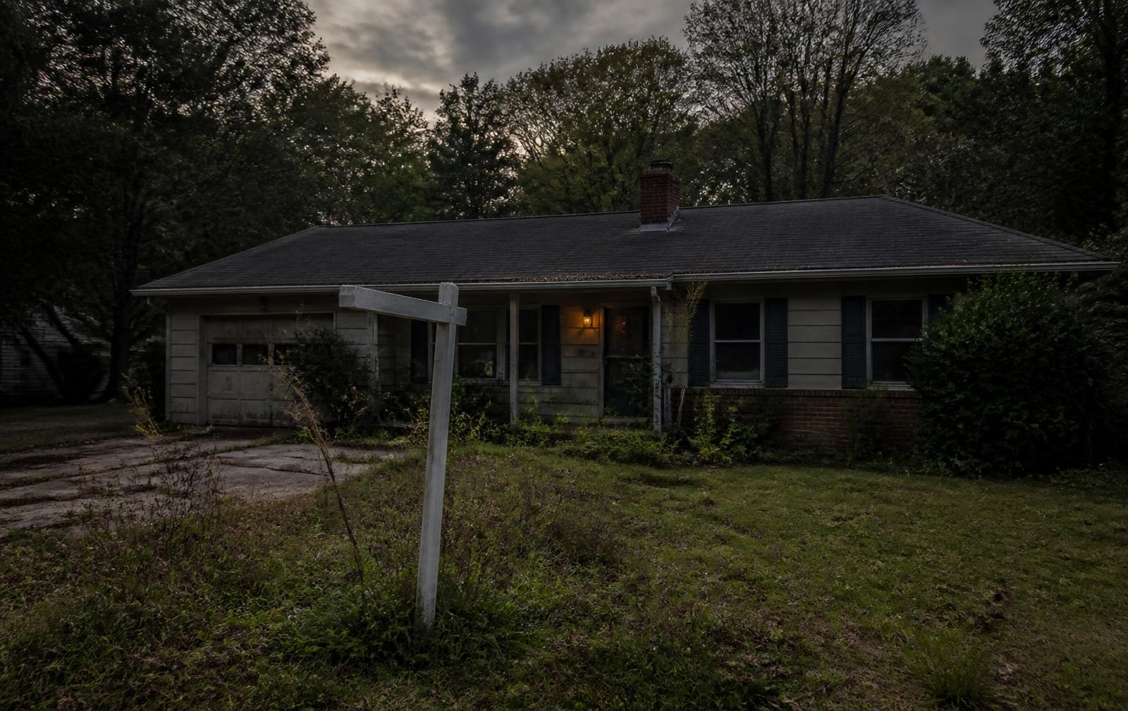 Weathered ranch house at dusk with a blank yard sign
